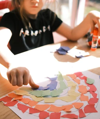 Child engaged in kindergarten collage making with colorful paper pieces