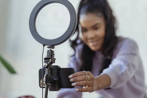 A woman setting up a smartphone on a tripod with a ring light. She is smiling and focused on adjusting the phone for recording.