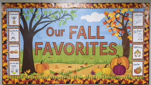 Bulletin board display with a fall theme titled 'Our Fall Favorites,' featuring large letters and seasonal decorations such as pumpkins, autumn leaves, and trees with colorful foliage. The display includes illustrations of students' favorite fall activities, set against a background of a fall landscape with a decorative border of autumn leaves.