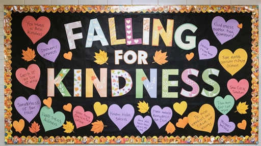 Bulletin board display with a fall theme titled 'Falling for Kindness,' featuring colorful letters and heart-shaped notes with messages about kindness. The board is decorated with autumn leaves and is set against a black background with a decorative fall-themed border.