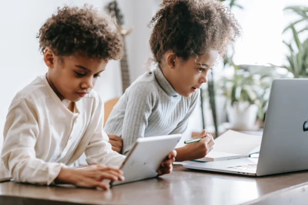 Two children using a tablet and laptop for a coding activity.