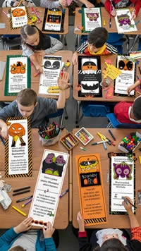 An overhead view of a classroom where students are decorating large Halloween-themed bookmarks, surrounded by colorful markers and craft supplies.