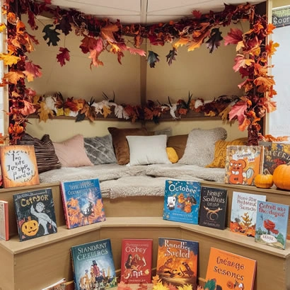 A cozy reading nook decorated with autumn leaves, pumpkins, and a selection of Halloween-themed books, creating a festive atmosphere for reading.